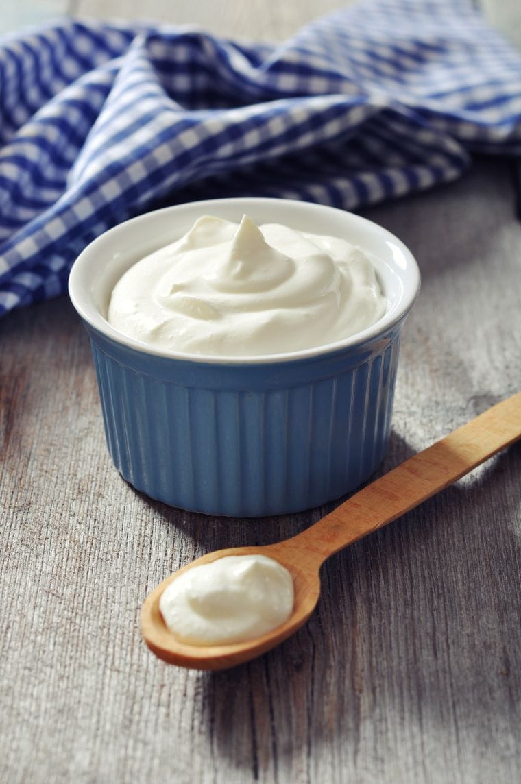 Greek yogurt in a ceramic bowl with spoons on wooden background